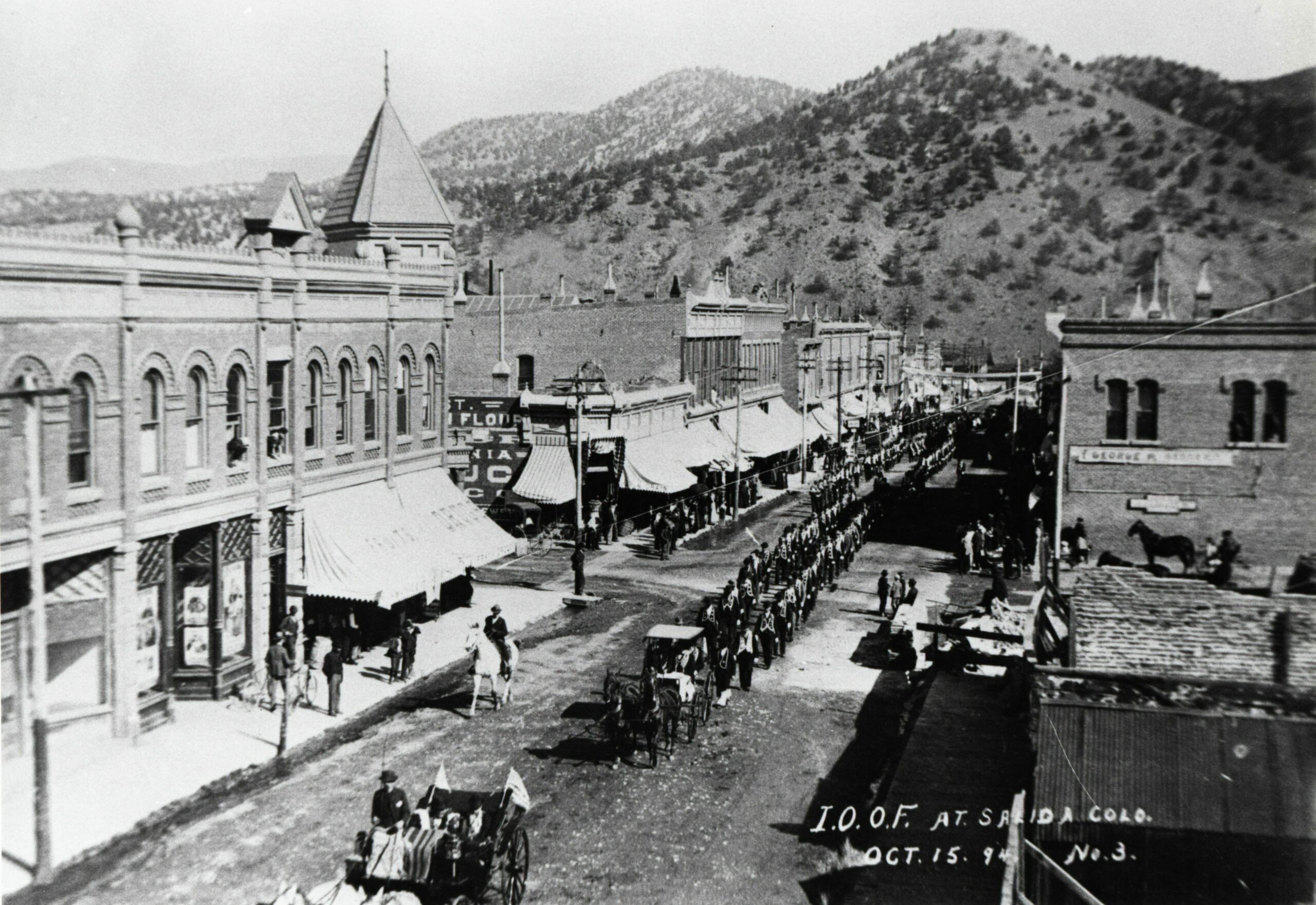 The International Order of Odd Fellows – during a statewide convention – parade up F Street October 15, 1894, preceded by dignitaries in carriages and followed by one of Salida’s marching bands. Cantons of the Independent Order of Odd Fellows perform military-style drills for prizes in a parade up F Street Oct. 16, 1894. The group held its Grand Encampment in Salida Oct. 15-18, 1894, complete with military-style parades, lodge meetings and dances organized by its ladies’ division, the Daughters of Rebekah.  Six years after the disastrous 1888 fire, there appears to be construction work in the lot on the corner of Second and F Streets where the Knights of Pythias building stands today. Alger’s Drug Store is in the J. M. Collins building (with the large awning) at the left. In 2001 this is the parking lot for Pueblo Bank and Trust.  (1)