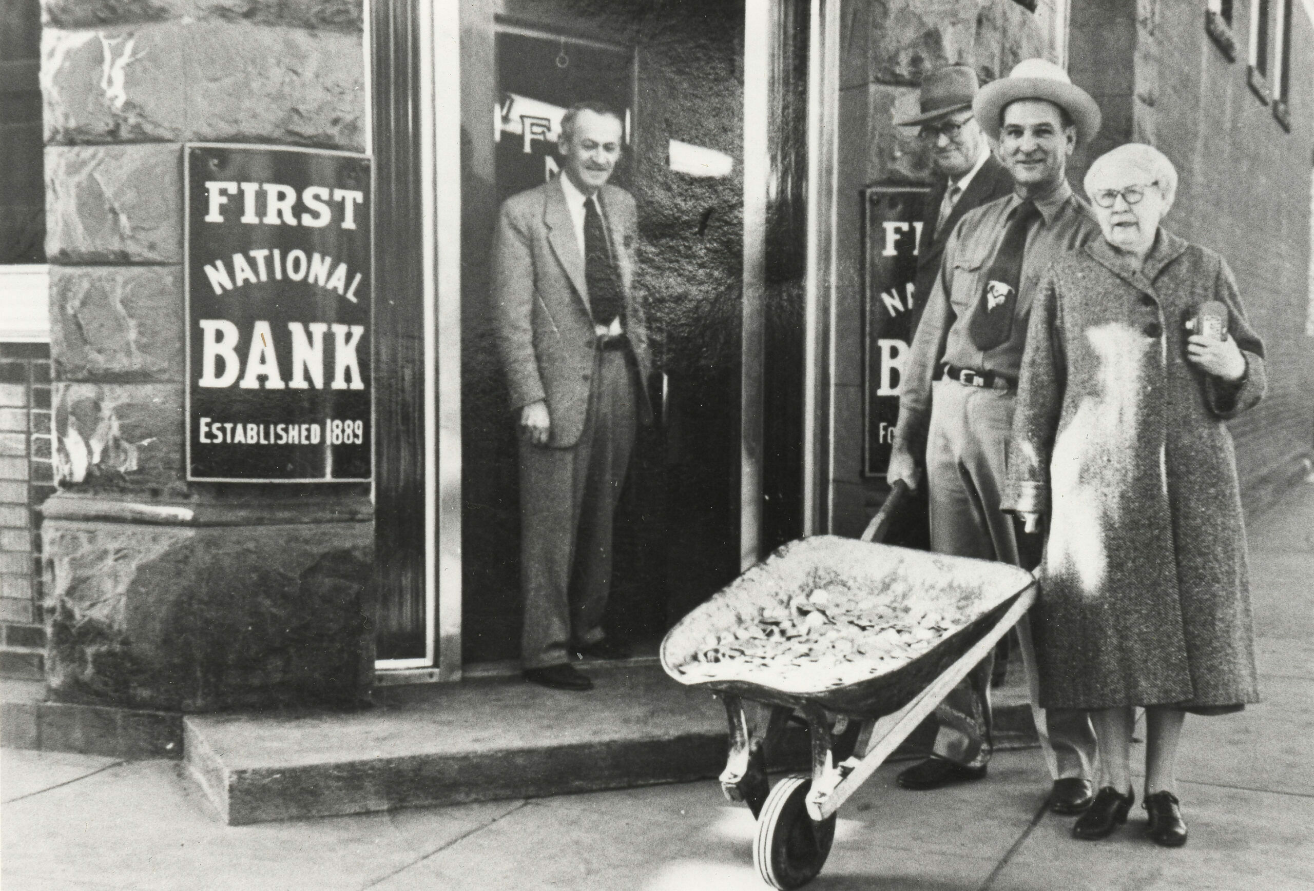 February 25, 1954 – J. Ford White, C. H. Kelleher (President, Salida Building and Loan Association), Theo. M. Jacobs, Alice Chinn (Secretary/Treasurer, Salida Building and Loan Association). A patron of the Building and Loan had paid off a mortgage with this wheelbarrow load of silver dollars. Building and Loan officers are shown on the way to deposit the silver dollars at First National Bank.