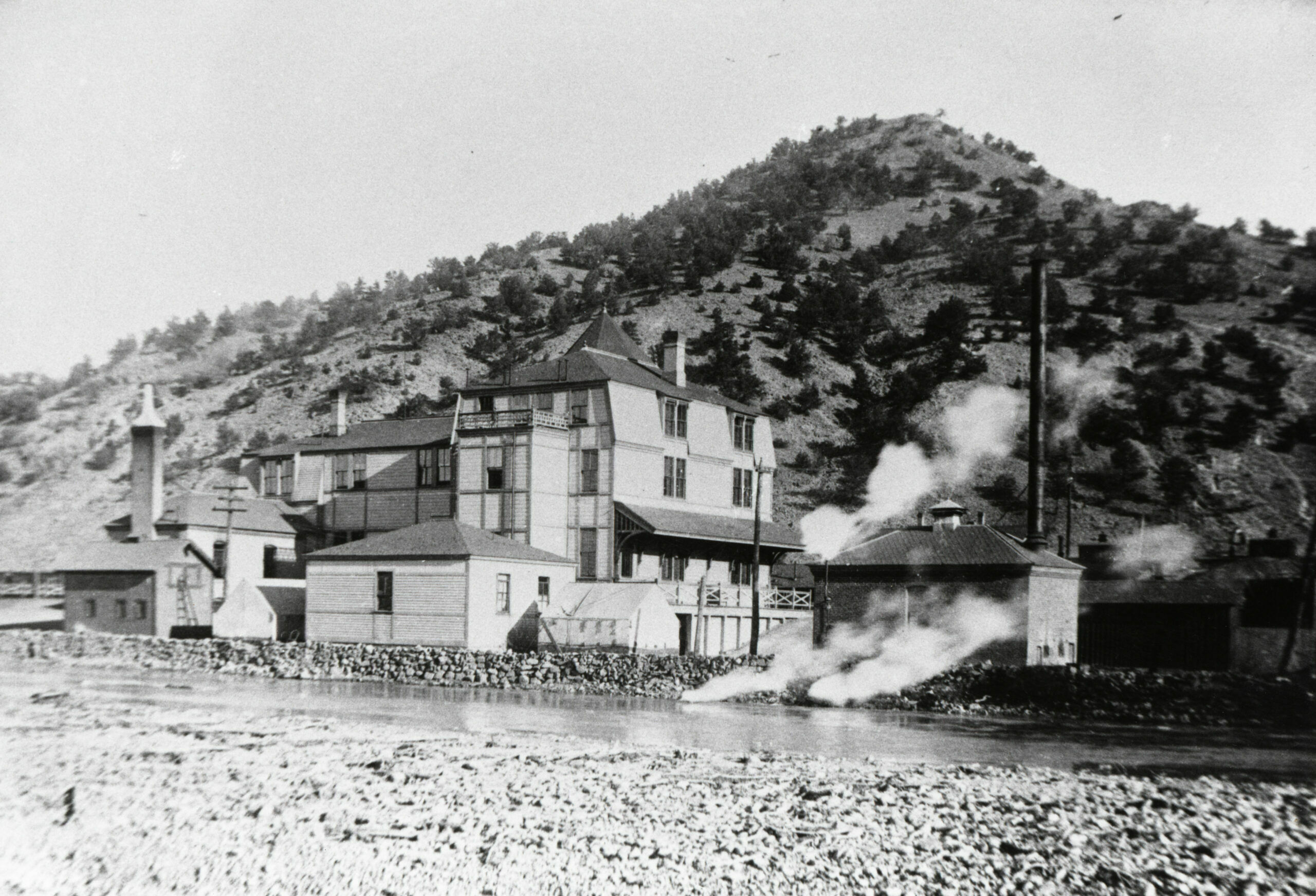 The rear of the Hotel Monte Christo is seen in this rare view, recorded on a glass negative before 1889, during the period before the standard-gauge reached Salida. Tents were put up for additional staff on either side of the bunkhouse. The D&RG pumphouse is to the right of the hotel. Beyond the pumphouse coal shed, the cabooses are visible. A protective rock wall was built to prevent erosion of the property by high water from the Arkansas River. Tenderfoot Hill, still speckled with pinon and cedar trees, was beyond the hotel and railroad yards.  (2)