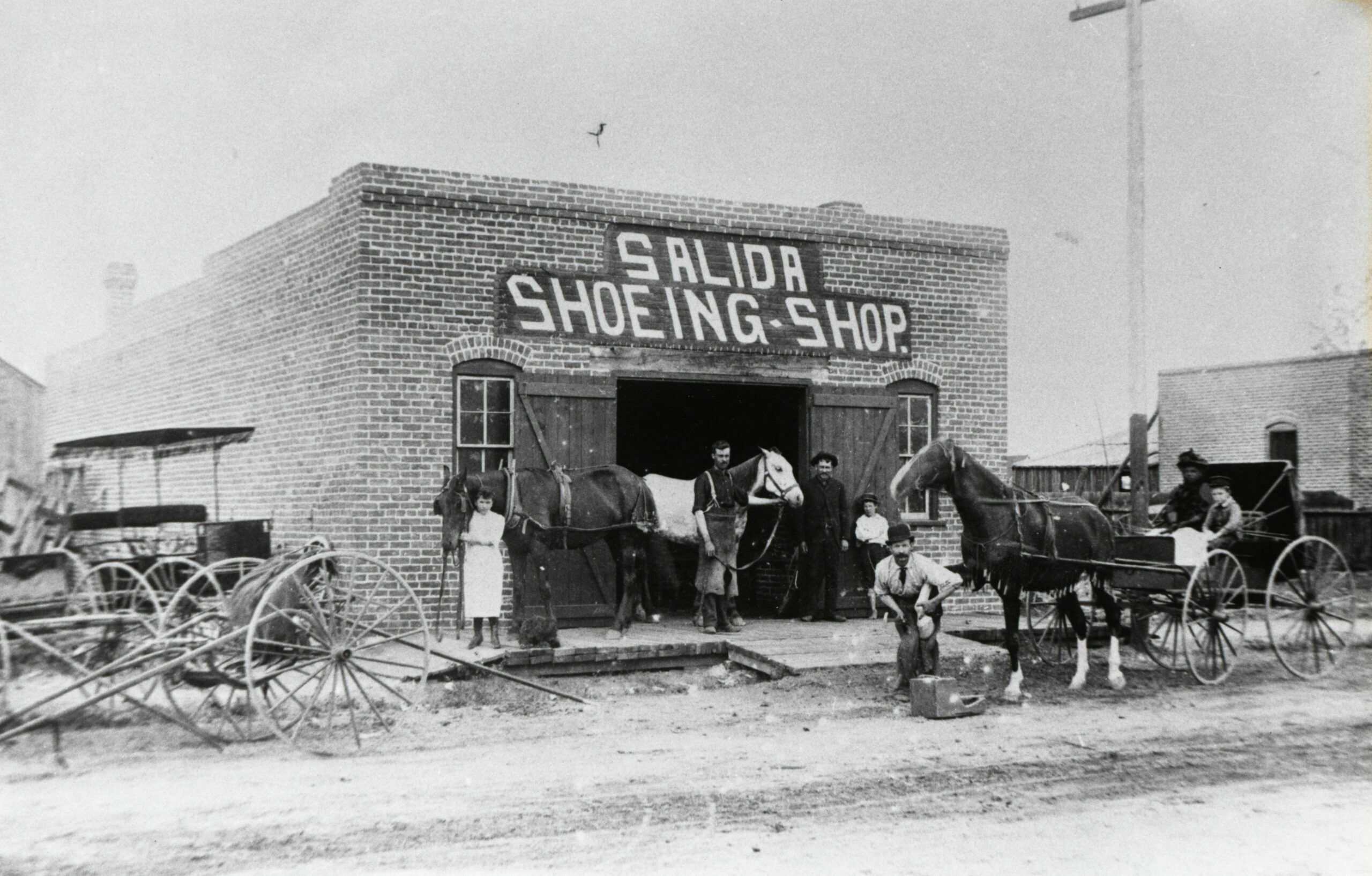 This horseshoeing business had the financial backing to locate in a brick building – much preferred after the 1888 fire – which is said to have been located between First and Second streets on G Street (at the corner of the alley). Netting was draped over the body of a horse to ward off flies and mosquitoes, terrible pests for both horses and people in the days before sanitation and mosquito-control districts. Used buggies were in the lot beside the shop.  (2)