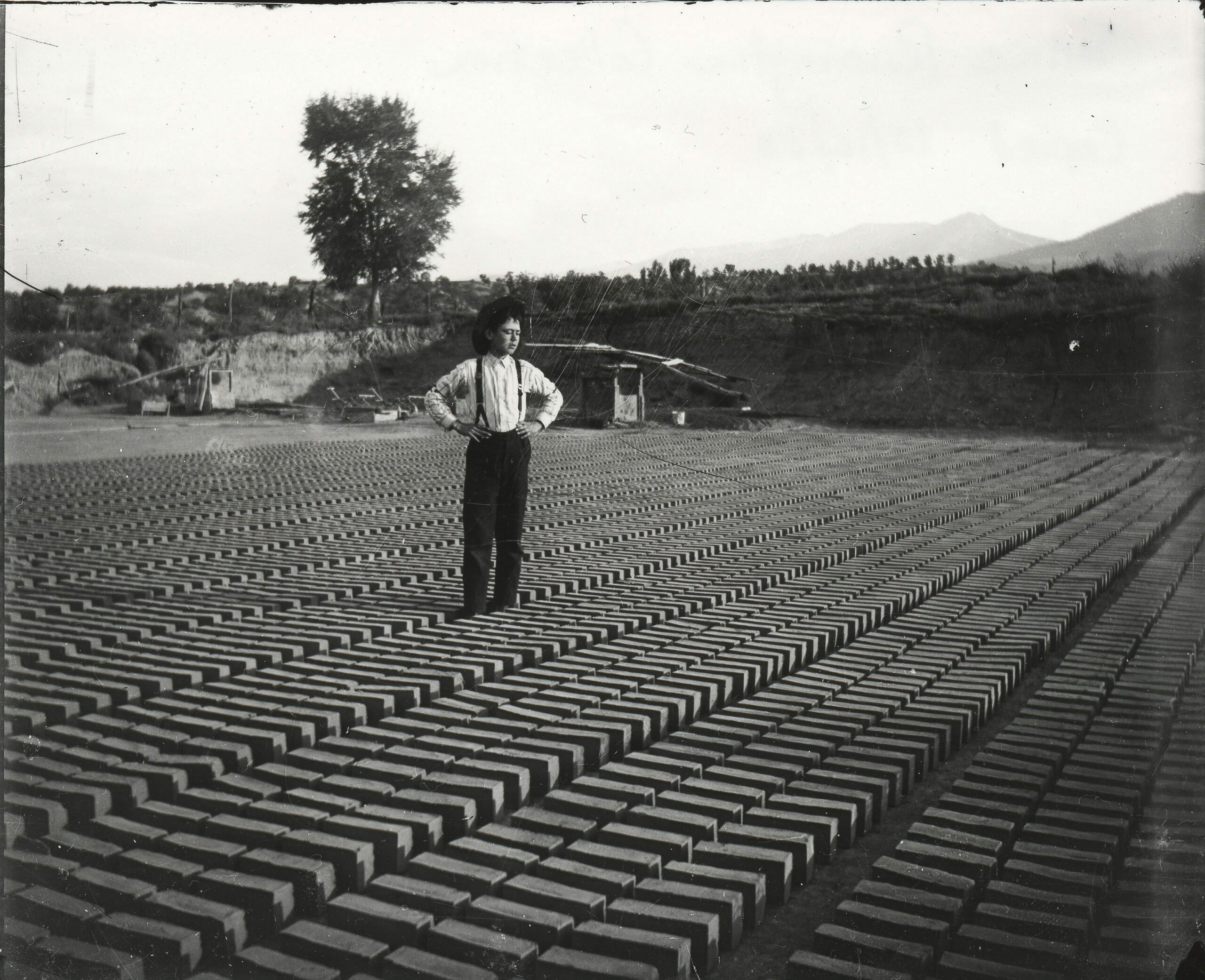 Bricks drying in the sun. Clay was packed into three-brick molds which were then dumped on the ground in long rows to sun dry. This unidentified boy may have been responsible for the thousands of bricks drying around him. Most of Salida’s buildings are made of this soft, red local brick.  (1)