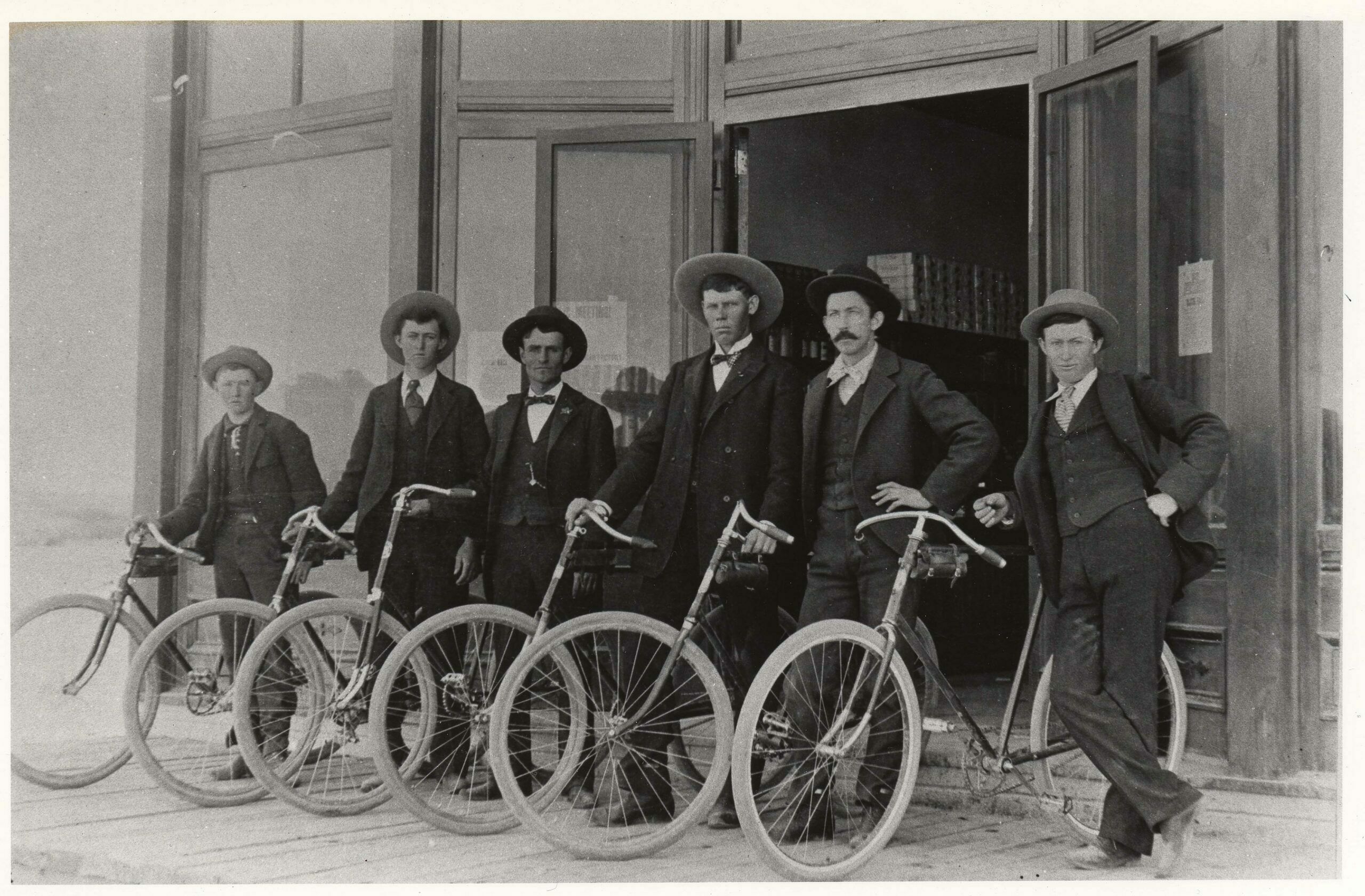 Young men took to bicycles in the early 1890’s like they do to cars and pickup trucks today. As with bicyclists today, the clothing had to fit the sport, and it was suits, ties, hats and vests – Sunday finery. Most were equally comfortable on these “safety” bikes or on the high-wheel “ordinaries.” They formed riding clubs, held a variety of endurance and short distance contests, and sometimes managed to rub parents and law officers the wrong way with their speed and crazy antics. This photo was taken in front of the I.O.O.F. Hall, Phil Bogler is third from the left.  (1)